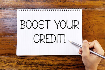Boost your credit handwriting text on blank notebook paper on wooden table with hand holding pencil. Business concept about boosting your credit.