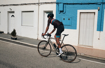 Fototapeta premium Professional male cyclist in racing gear on a road bike, against urban houses.Quick trip around the city on a bicycle.