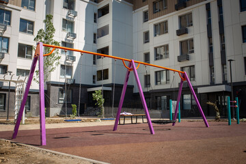 A new colorful playground in a sunny summer courtyard among residential high-rise buildings