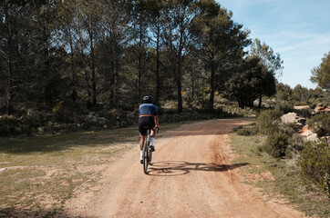 Men riding gravel bike on gravel road in mountains with scenic view  in Alicante region.Man cyclist  wearing cycling kit and helmet.Beautiful motivation image of an athlete.Alicante, Spain