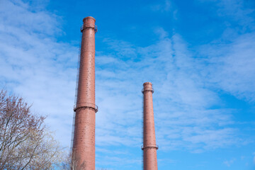 Two tall abandoned industrial chimney pipes against blue sky. Chimneys an industrial plant. Smoke pipes. Smoke tubes. Factory pipes pipes made of bricks.