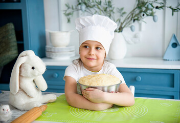 little cute girl wearing a white chef's hat and uniform holding a bowl of dough for easter bread in the blue and white kitchen