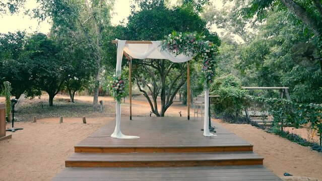 Chuppa with the flowers for a wedding ceremony under the sky in the orchard during the day.