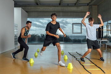 Teenagers and instructor performing circuit routine functional training at the gym. Male coach and...