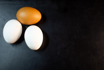 Two white eggs and one brown egg on a black background
