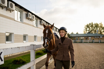 Attractive smiling woman equestrian walking horse in outdoor paddock