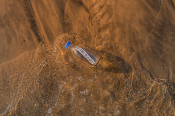 glass bottle with message save the planet inside on the seashore washed away by the waves at sunset