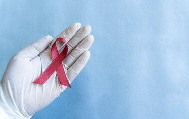 Oral Head and Neck Cancer Awareness ribbon image, white glove hand holding maroon colour ribbon