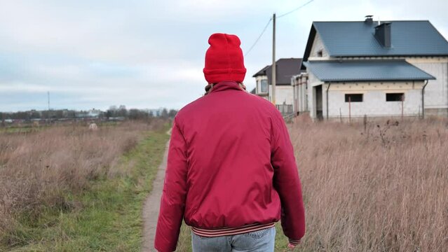 A sad teenage girl in red clothes is walking down the street. View from the back.