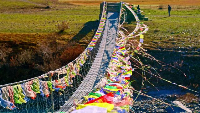 Many Buddhist Tibetan prayer flags on a footbridge blowing in the wind in slow motion