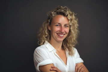 Femme de type européen souriante en chemisier blanc les bras croisés sur fond sombre