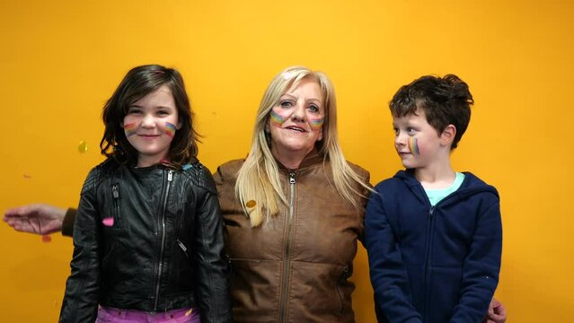 grandmother and grandchildren paint a rainbow on each other's cheeks. lgbt flag