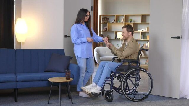 Man in wheelchair extend her hand palm up to side. Woman giving key with keychain from new house for handicapped