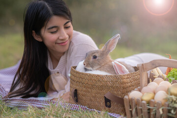 Cute fluffy brown hair easter rabbit in basket look away while owner look at her own pet with smile of love and happiness. Pet care concept with blur green background.