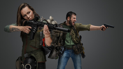 Fototapeta na wymiar Studio shot of woman aiming rifle and screaming guy in setting of post apocalypse.