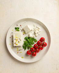feta cheese, for salads, with cherry , green butter, greens, on a white plate, appetizer, top view, close-up,