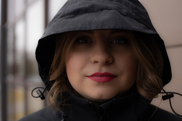 A woman with red lips in a black hoodie under the rain. Beautiful young woman under the hood. Young girl with beautiful red lips