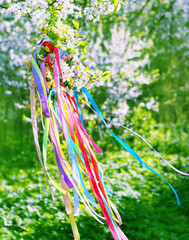 Spring floral wreath with colorful ribbons on tree in garden, green natural background. floral decor. Symbol of Beltane, Wiccan Celtic Holiday beginning of summer. witchcraft traditional ritual. - obrazy, fototapety, plakaty