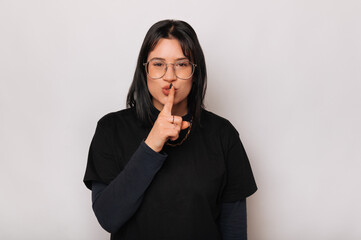 Young cute woman wearing black is holding finger on the lips for silence.