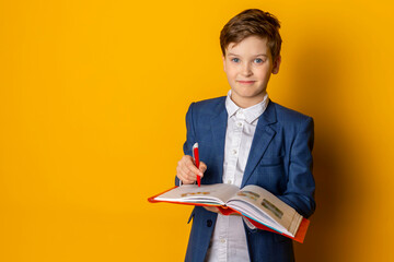 A little boy in a blue suit and white shirt, neatly dressed, attentively doing his homework,...