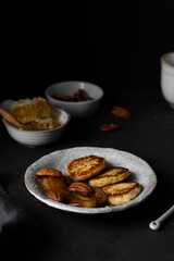 Cottage cheese pancakes, syrniki, ricotta fritters on ceramic plate with honey, nuts and backed bananas on a dark background. Healthy breakfast.