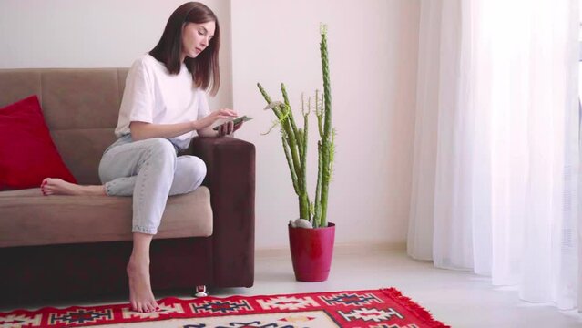 Young beautiful woman blogger florist sit on sofa at home,holding smartphone and take photo for social media to tell about plant diseases.Indoor plants diseases disorders Identification and treatment