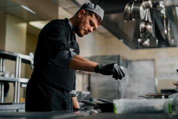 Professional kitchen in hotel restaurant close-up chef squeezes lemon on spinach on pan