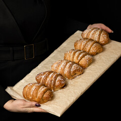 Puff pastry buns. Fresh pastries on parchment paper inhands of woman. Puff cakes sprinkled with powdered sugar. Black background. Top view. 