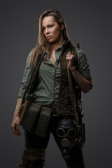 Portrait of military woman with rifle in post apocalyptic setting against grey background.