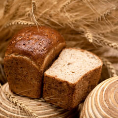 Homemade bread with flax seeds from wheat flour. Healthy diet. Loaf of bread in shape of brickin cut form on wooden stand among spikelets of wheat. Grain harvest. Soft focus, side view. 