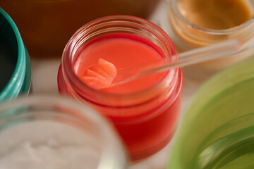 Red plastic jar and spoon with lip balm product close up. Health and skin care morning routine....