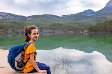 A child with a backpack looks at a beautiful mountain lake. Relaxed, peaceful, thoughtful, happy and free on a mountain lake.