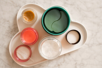 Skin care products on white ceramic tray with eye patches and face mask on marble table top view close up. Health care products. Selective focus.