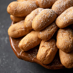 Small oval buns made from wheat flour for breakfast. Pile of buns on plate sprinkled with powdered sugar. Fresh homemade cakes. Gray background. Close-up. View from above. Soft focus.