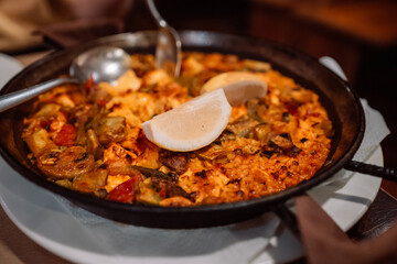 Classic dish of Spain, seafood paella in traditional pan on rustic blue concrete background . Spanish paella with shrimps, clamps, mussels, green peas and fresh lemon wedges from above 