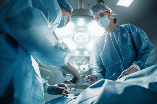Shot of three surgeons dressed in robes and masks with patient in operating room.