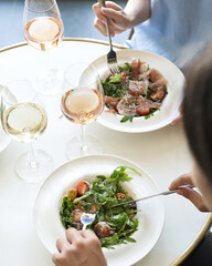 Women dine in restaurant and drink wine. Glasses of white wine and plates with salad on round white table. Light lunch. Italian restaurant. Healthy food. Fitness menu. View from above.
