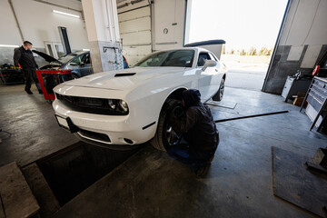 Mechanic in service repair station working with muscle car.  Man worker jacks up the car to diagnose the chassis.