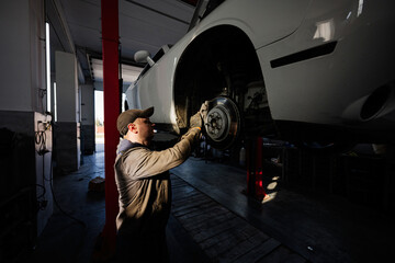 Mechanic in service repair station working with muscle car in lift at sunset shadows.