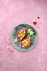 Obraz na płótnie Canvas Traditional Valentines Day fruit salad with exotic fruit pieces served in dragon fruit bowls and decorated with star fruit on a Nordic design plate as top view with text free space