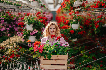 Young woman working in a greenhouse and holding wooden box full with flowers