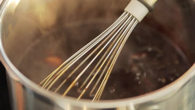 whisk in a boiling pot. Heating crushed pecan nuts and melted chocolate. Chocolate bubbles boiling in a stainless steel pot with whisk stationary in the center. boiling chocolate