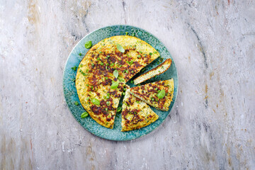 Traditional Italian vegetable frittata with zucchini, onion and cheese served as top view on Nordic design plate with text space