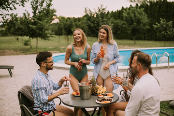 Group of young people cheering with cider by the pool in the garden