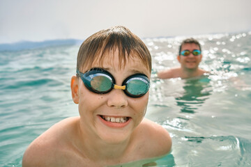 Happy family in swimming goggles, father and son bonding, play, swim in the sea looking at view enjoying summer vacation. Togetherness Friendly concept
