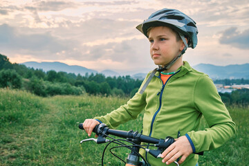  Happy cute boy in helmet learn to riding a bike in park on green meadow in summer day at sunset time. Family weekend.