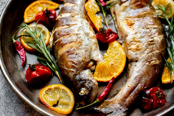 baked trout with lemon, orange, spices on a stone background