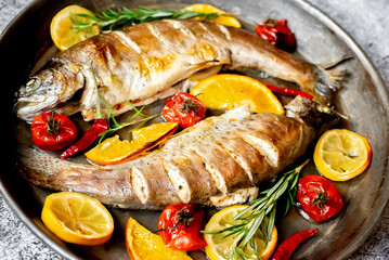 baked trout with lemon, orange, spices on a stone background