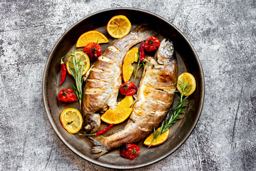 baked trout with lemon, orange, spices on a stone background