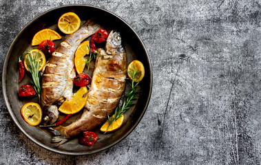 baked trout with lemon, orange, spices on a stone background with copy space for your text